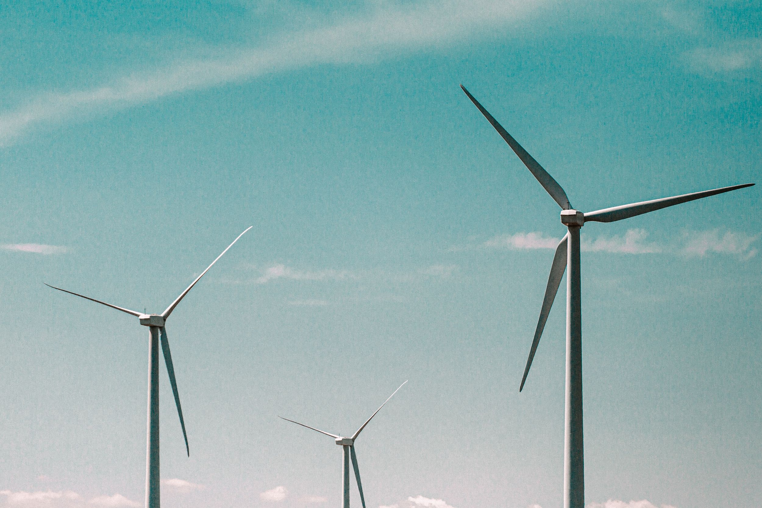 Three wind turbines stand against a clear blue sky with wispy clouds, highlighting renewable energy sources.