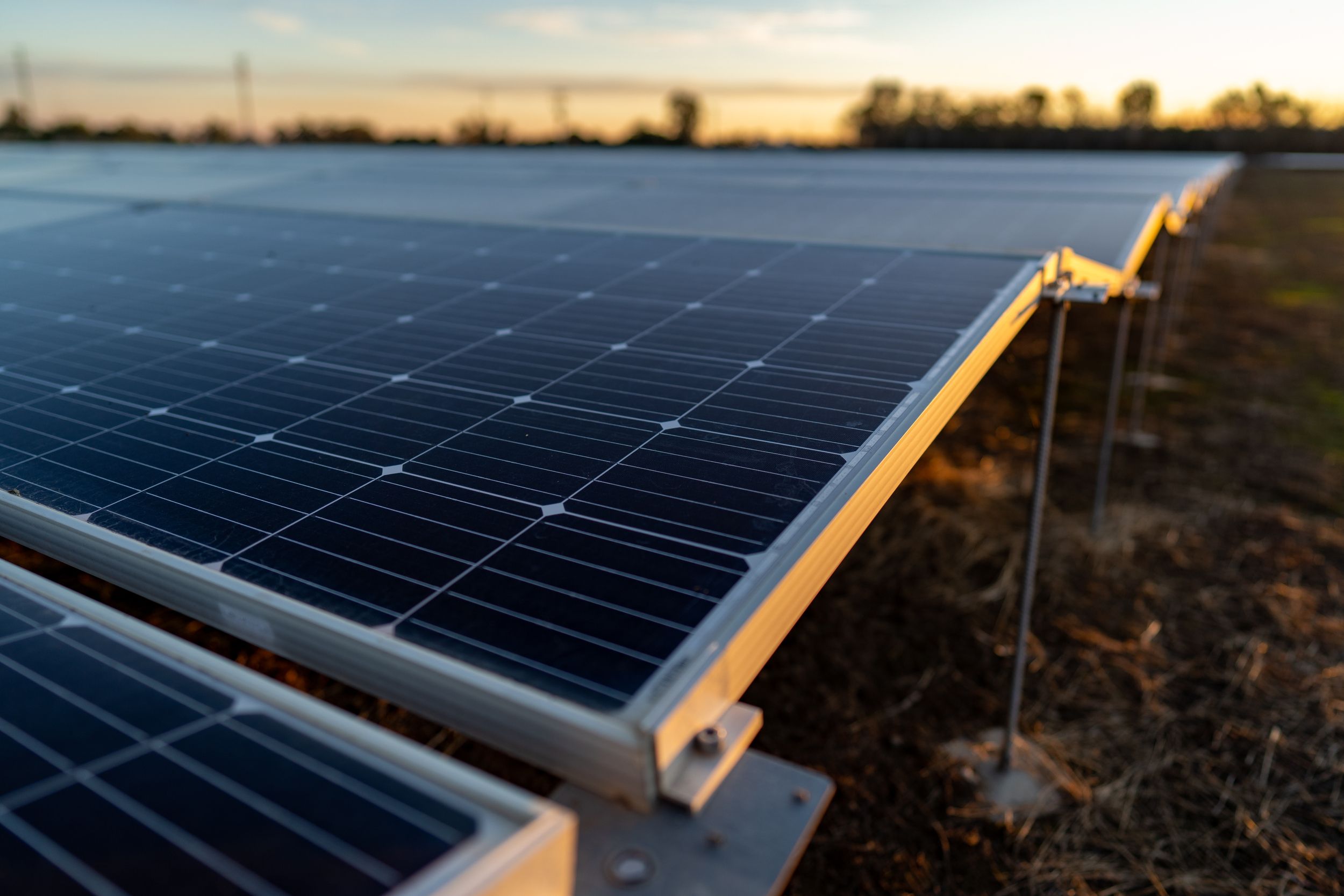 Close-up of solar panels in a field during sunset, showing reflective surfaces and metal supports.