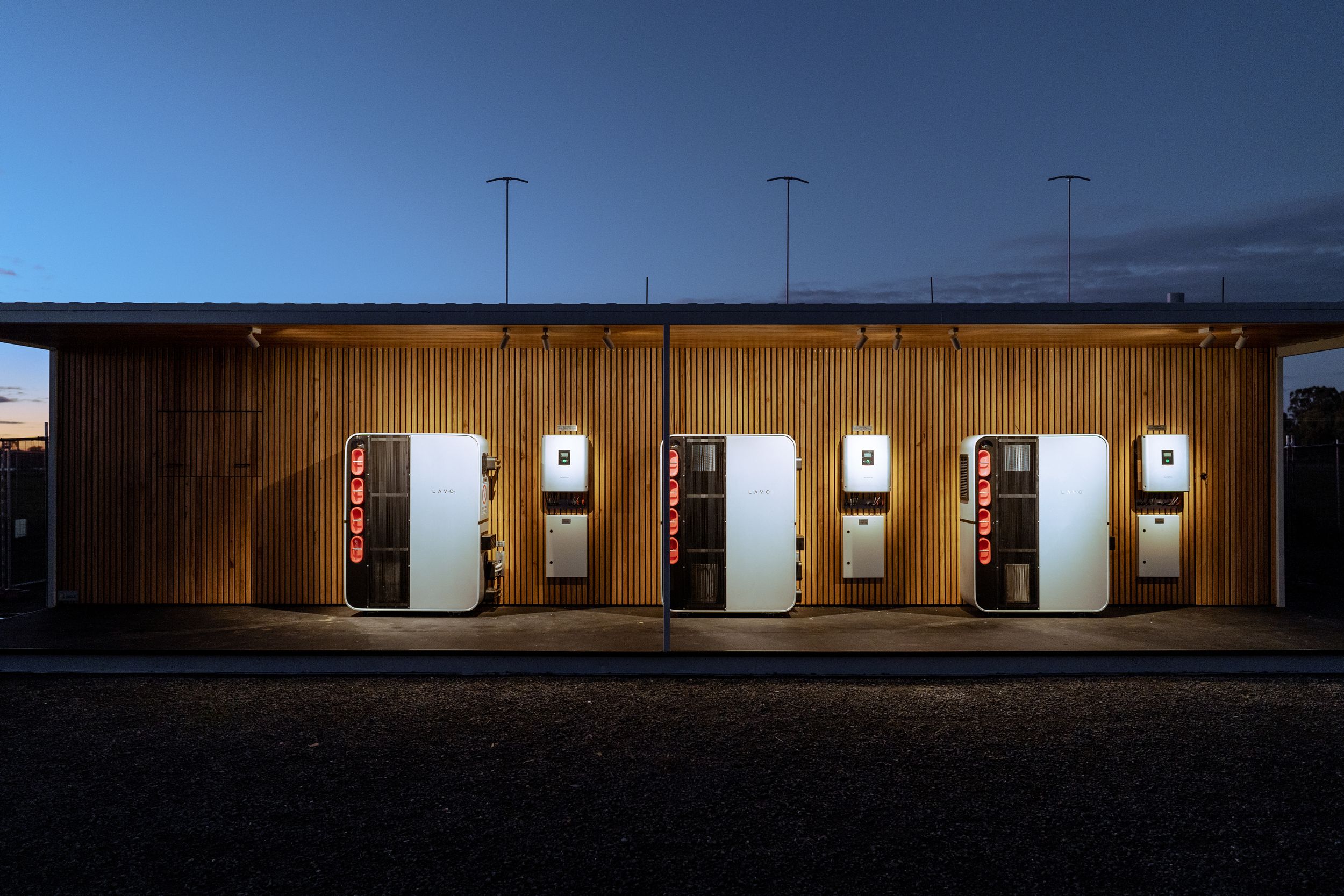 A modern wooden structure at dusk with several illuminated vending machines against a darkening sky.